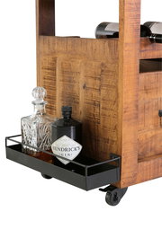 Nahaufnahme eines rustikalen Servierwagens aus Holz mit Flaschenablage, gefüllt mit einer Kristallkaraffe und einer Gin-Flasche, auf Rollen.