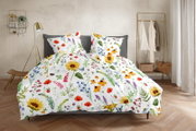 Bettwäsche-Set mit weißem Hintergrund und farbenfrohem Wildblumen- und Sonnenblumenmuster, frontal in leichter Schrägansicht auf einem grauen Bett im Schlafzimmer inszeniert