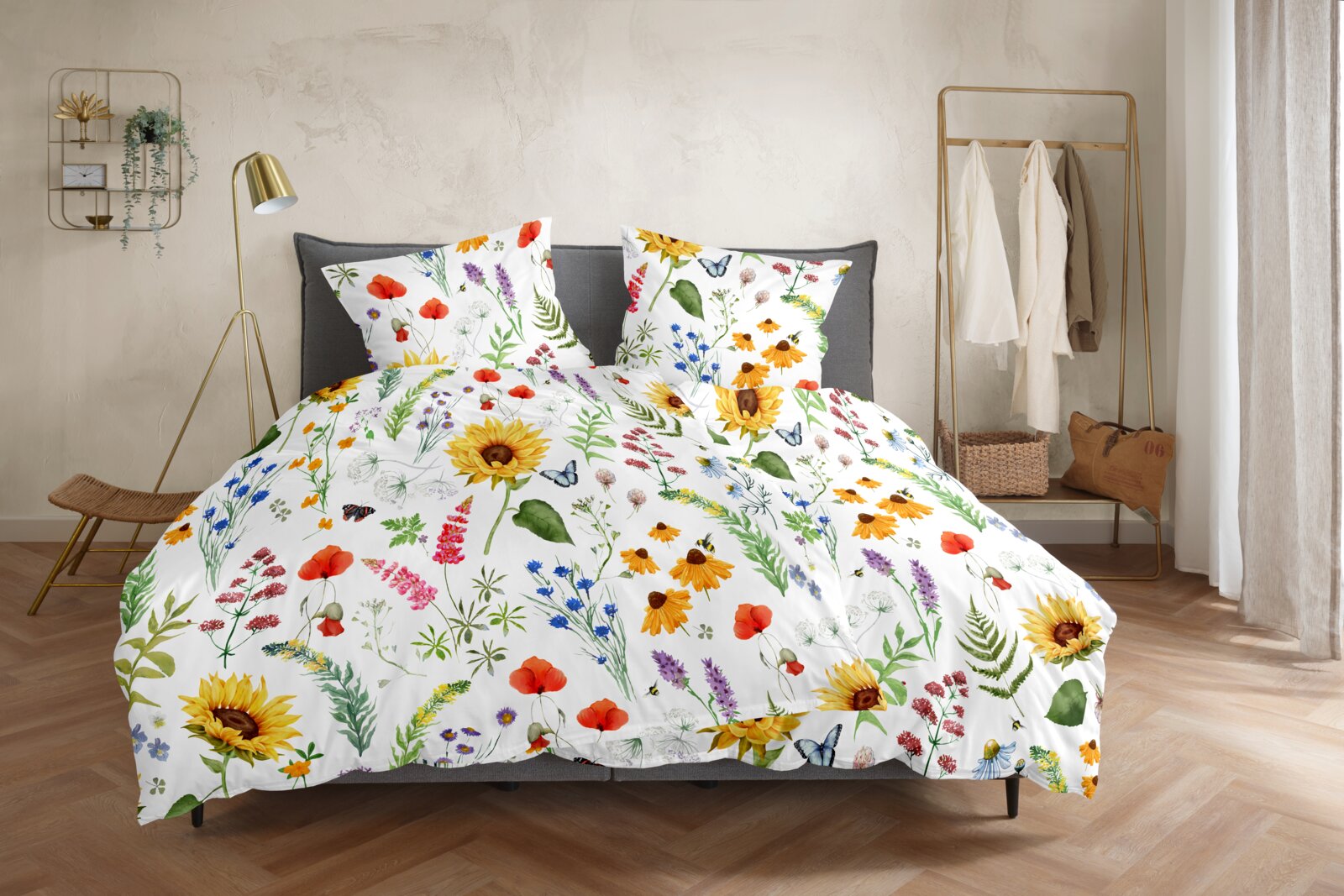 Bettwäsche-Set mit weißem Hintergrund und farbenfrohem Wildblumen- und Sonnenblumenmuster, frontal in leichter Schrägansicht auf einem grauen Bett im Schlafzimmer inszeniert