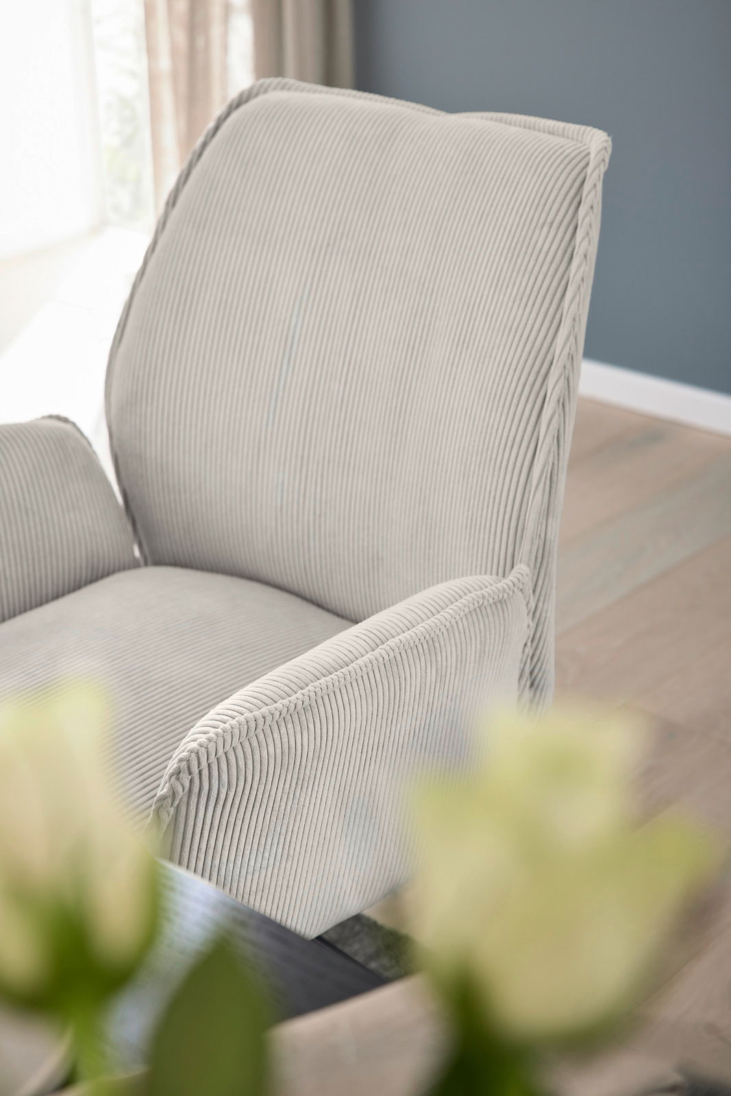 Nahaufnahme eines Armlehnstuhls mit hellgrauem, geripptem Stoffbezug, seitliche Perspektive