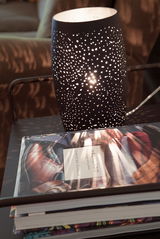 Tischleuchte Colby in sand-schwarz mit perforiertem Muster, das ein stimmungsvolles Lichtspiel erzeugt, seitliche Perspektive.