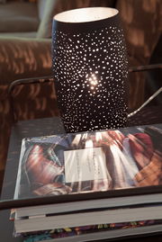 Tischleuchte Colby in sand-schwarz mit perforiertem Muster, das ein stimmungsvolles Lichtspiel erzeugt, seitliche Perspektive.