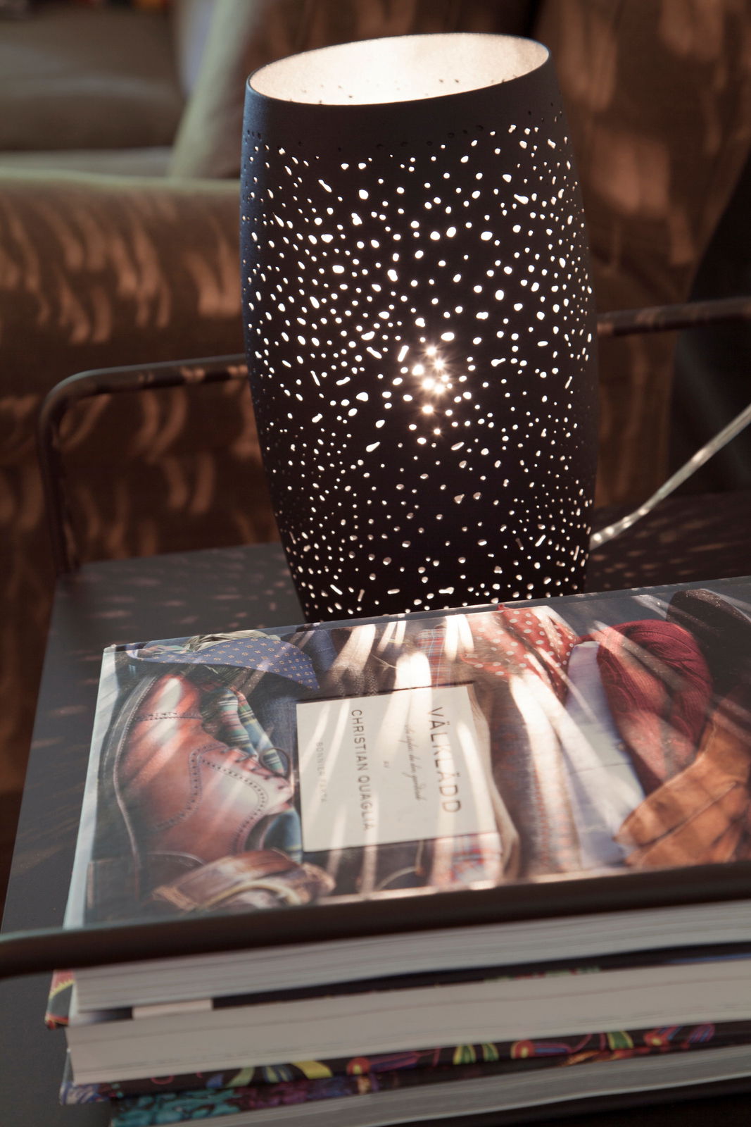 Tischleuchte Colby in sand-schwarz mit perforiertem Muster, das ein stimmungsvolles Lichtspiel erzeugt, seitliche Perspektive.