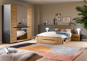 Modernes Schlafzimmer-Set in Holzoptik mit Bett inklusive Stauraum, Nachttisch und großem Kleiderschrank mit Spiegeltüren, aufgenommen in schräger Frontansicht aus leicht erhöhter Perspektive.