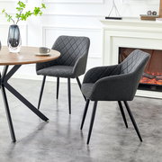 Zwei dunkelgraue, rautenförmig gesteppte Polsterstühle mit Armlehnen und schwarzen Metallbeinen an einem runden Holztisch im hellen Wohnraum, seitliche Perspektive