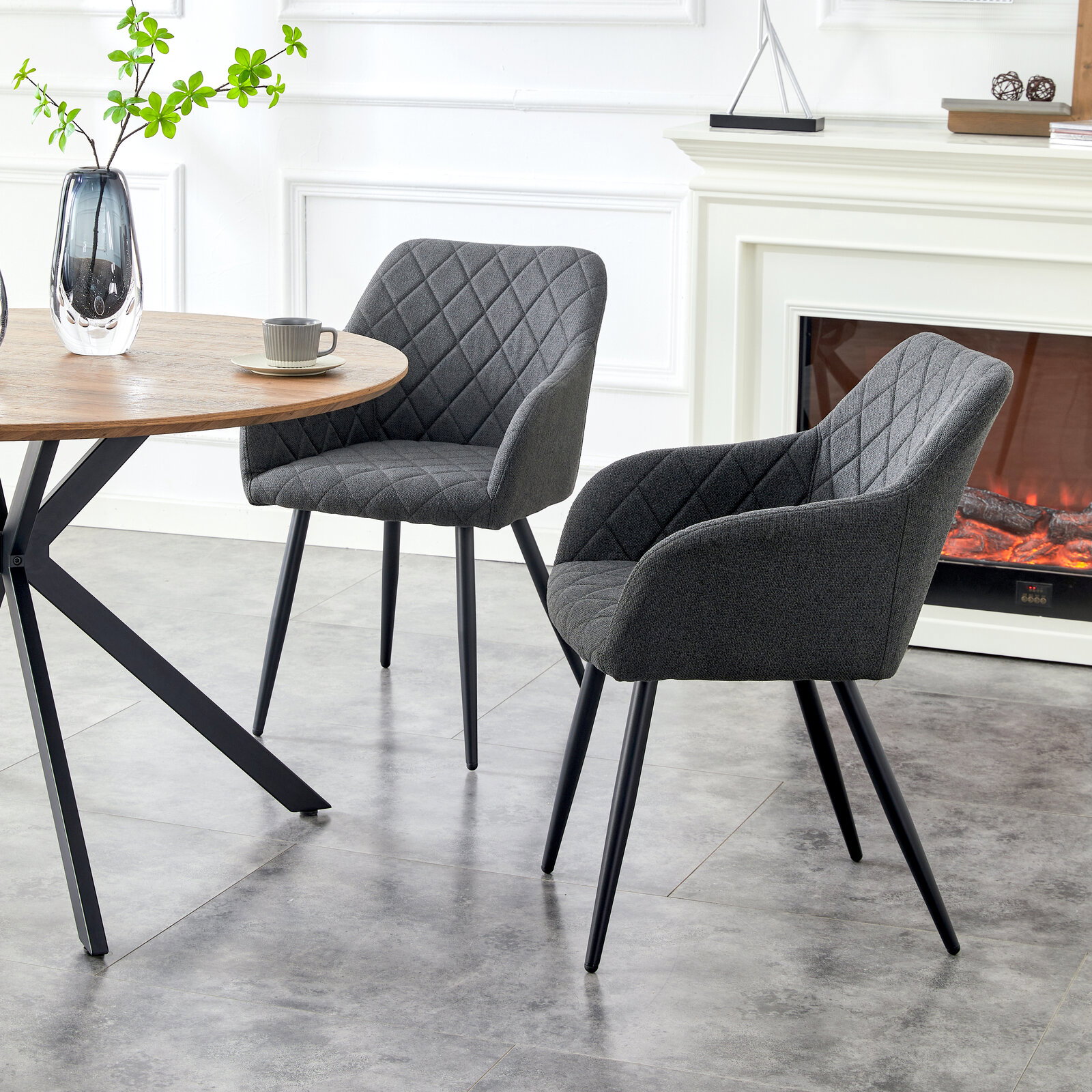 MID.YOU Stuhl 2er-Set LEA Zwei dunkelgraue, rautenförmig gesteppte Polsterstühle mit Armlehnen und schwarzen Metallbeinen an einem runden Holztisch im hellen Wohnraum, seitliche Perspektive