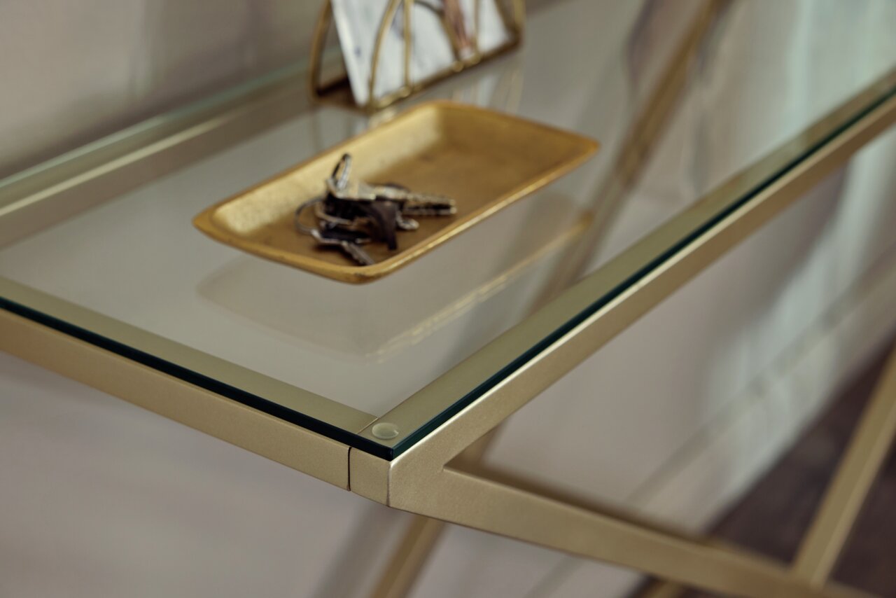 Nahaufnahme einer eleganten Konsole mit Glasplatte und goldfarbenem Gestell, darauf ein goldfarbenes Tablett mit Schlüsseln.
