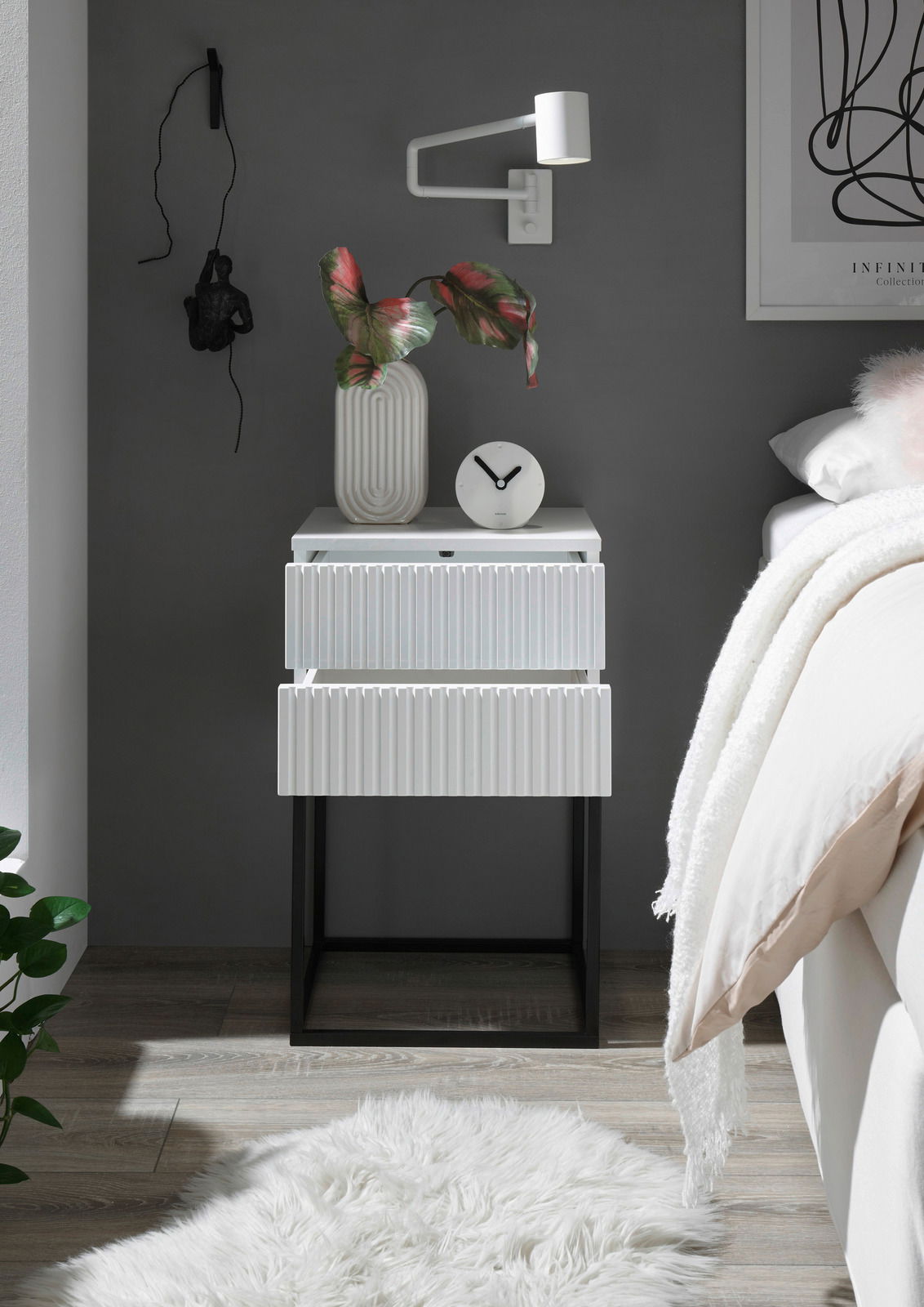 Moderne Nachtkommode mit zwei Schubladen in Weiß mit geriffelter Oberfläche, auf schwarzem Metallgestell. Perspektive: Frontalansicht.