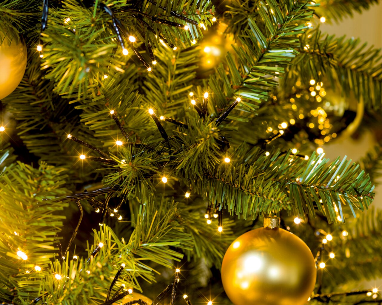 Nahaufnahme eines Weihnachtsbaums mit LED-Clusterbeleuchtung und goldener Kugel
