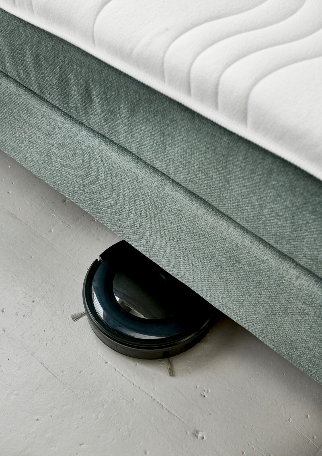 Boxspringbett BX 180/200 aus der Seitenperspektive mit einem Saugroboter, der darunter reinigt.