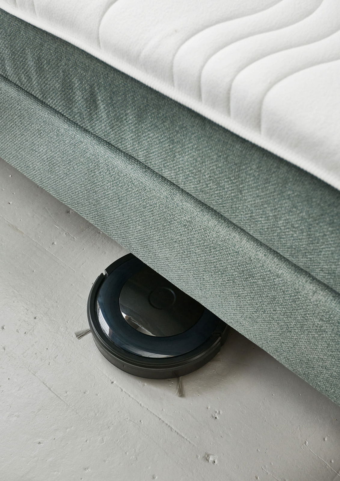 Boxspringbett BX 180/200 aus der Seitenperspektive mit einem Saugroboter, der darunter reinigt.
