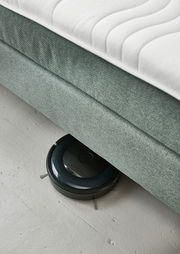 Boxspringbett BX 180/200 aus der Seitenperspektive mit einem Saugroboter, der darunter reinigt.