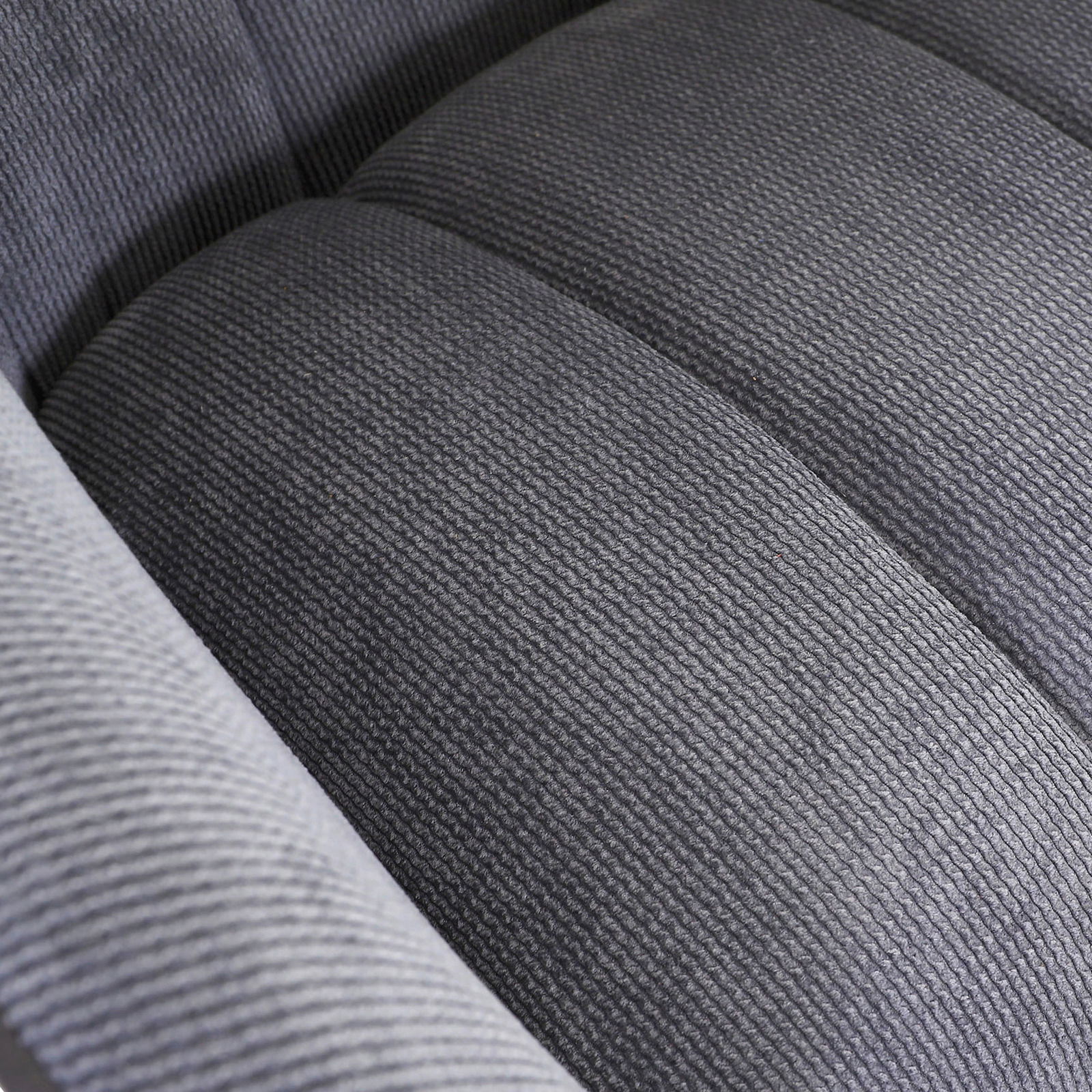 Nahaufnahme eines grauen, strukturierten Stoffes eines Armlehnstuhls, von oben betrachtet.
