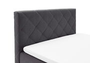 Seitliche Ansicht eines grauen Boxspringbetts mit gestepptem Kopfteil und weißer Matratze.