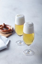 Zwei gefüllte Biergläser Daily mit Schaumkrone, von schräg oben fotografiert, neben einer Brezel auf einem Holzbrett.