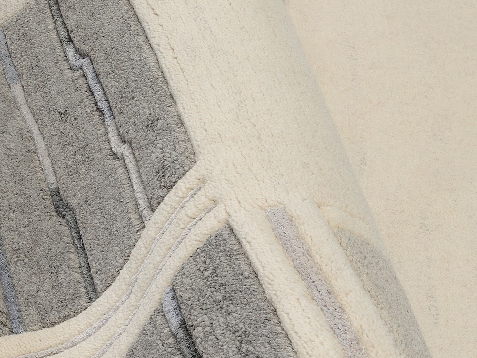 Nahaufnahme eines Wollteppichs mit grauen und cremefarbenen Mustern, perspektivisch von oben fotografiert.