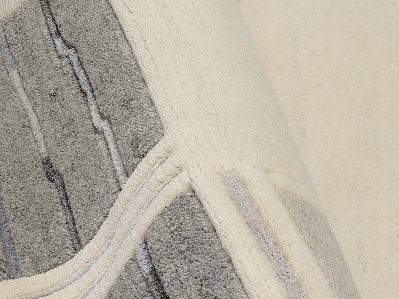 Nahaufnahme eines Wollteppichs mit grauen und cremefarbenen Mustern, perspektivisch von oben fotografiert.