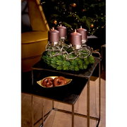 Schuin vooraanzicht van een zilverkleurige adventskandelaar met vier brandende mauvekleurige kaarsen, stijlvol gedecoreerd met dennengroen op een zwarte bijzettafel.