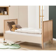 Kinderbett mit Holzgittern an beiden Enden, dekoriert mit einem Teddybär und Kissen, seitliche Perspektive
