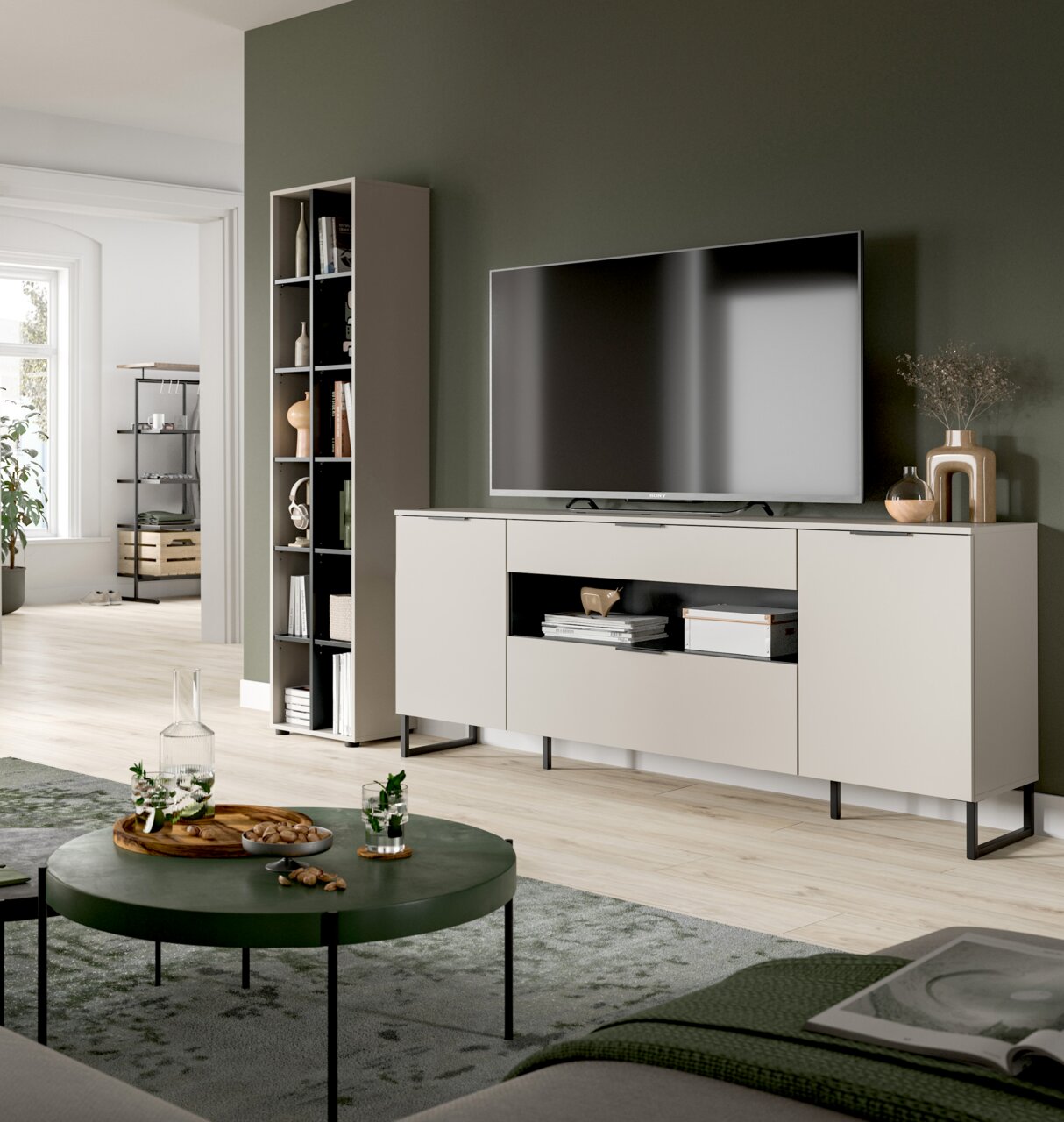 Modernes Wohnzimmer mit beigem TV-Lowboard auf schwarzen Metallfüßen und großem Fernseher, daneben hohes Regal; Aufnahme aus leicht schräger Frontperspektive.