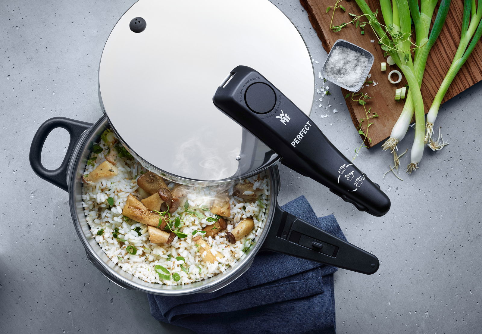 Draufsicht auf einen Schnellkochtopf mit Reis und Pilzen, umgeben von Frühlingszwiebeln und Salz.