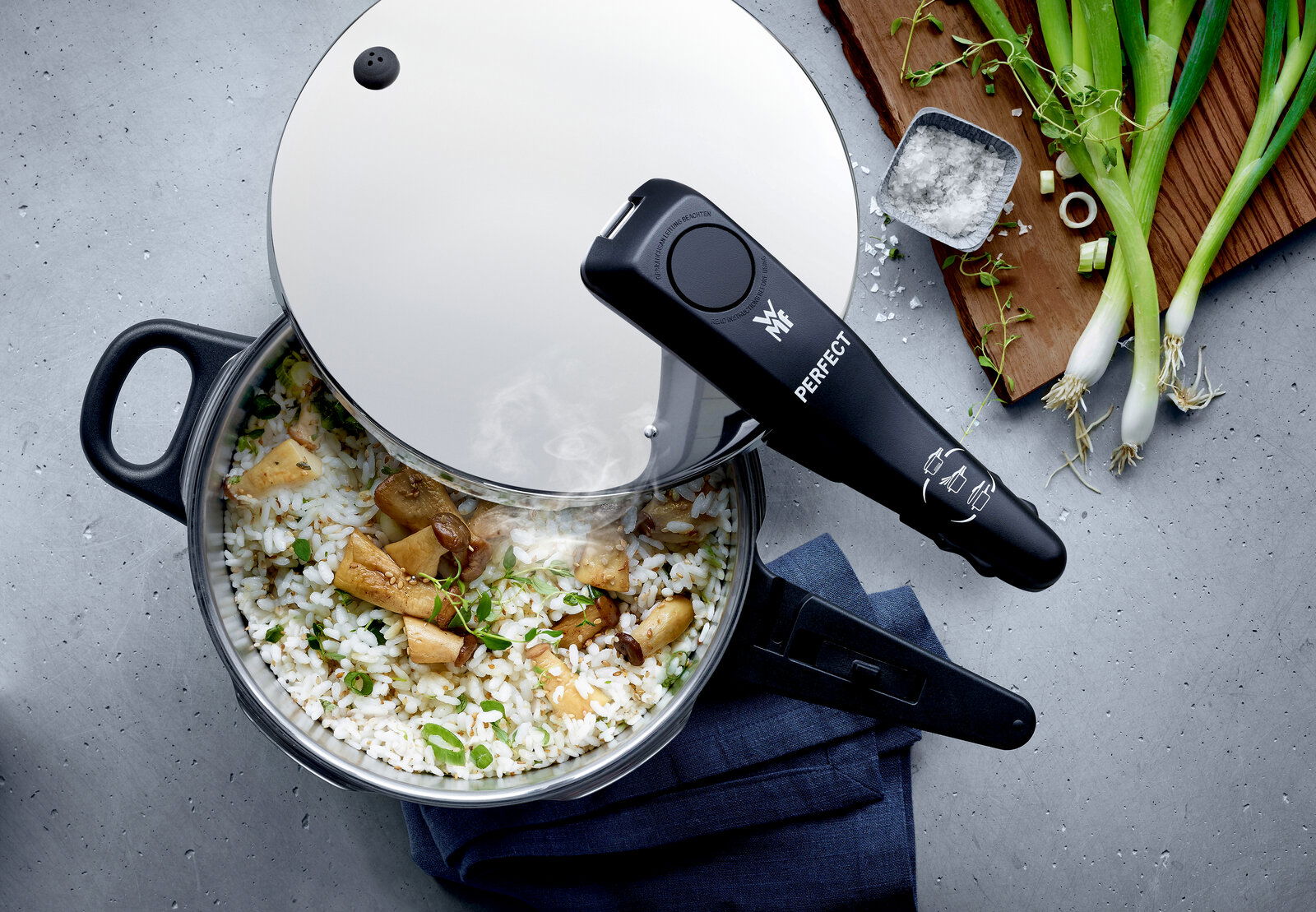 Draufsicht auf einen Schnellkochtopf mit Reis und Pilzen, umgeben von Frühlingszwiebeln und Salz.