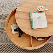 Ronde houten salontafel met draaibaar tafelblad, met daaronder opbergruimte met een koptelefoon en een notitieboekje, gezien van bovenaf.