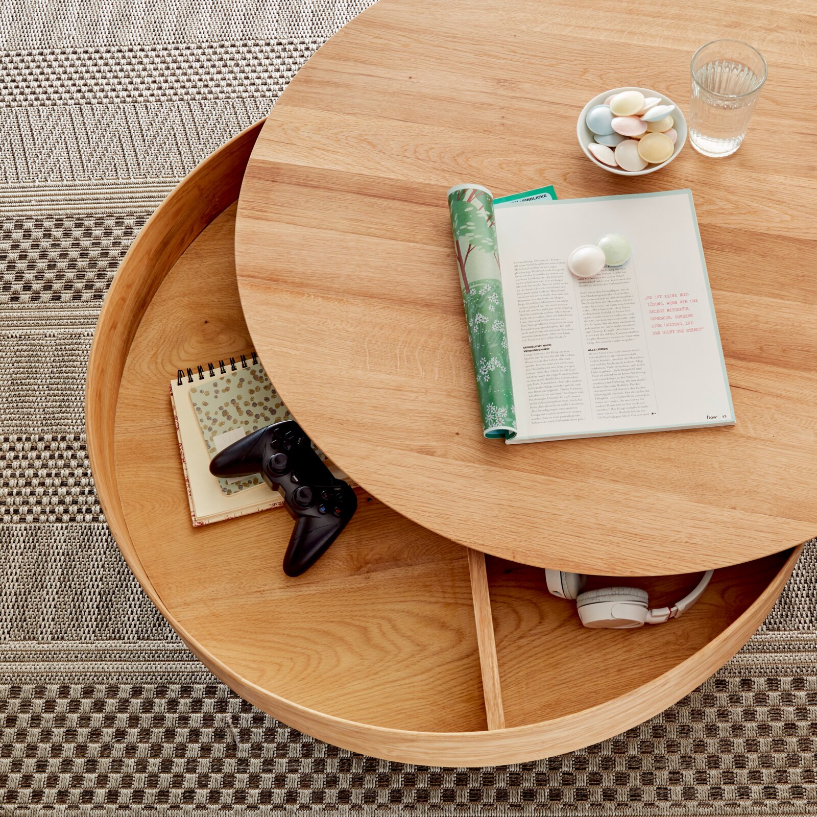 Ronde houten salontafel met draaibaar tafelblad, met daaronder opbergruimte met een koptelefoon en een notitieboekje, gezien van bovenaf.