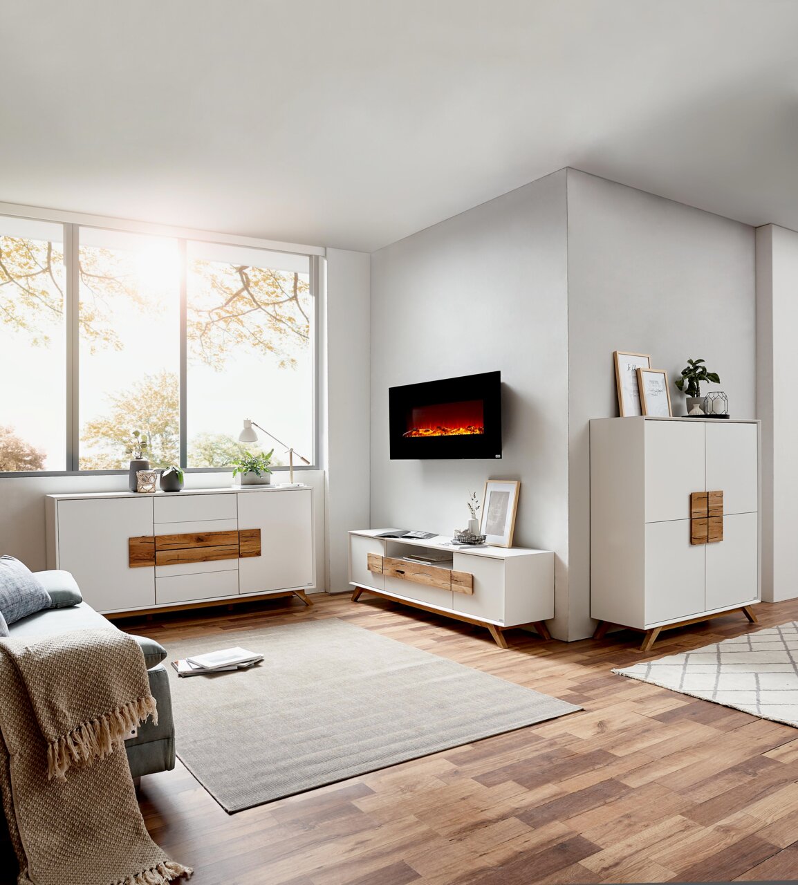 Modernes Wohnzimmer mit weißem Highboard, Sideboard und TV-Lowboard aus Holz und weißen Fronten, seitliche Perspektive