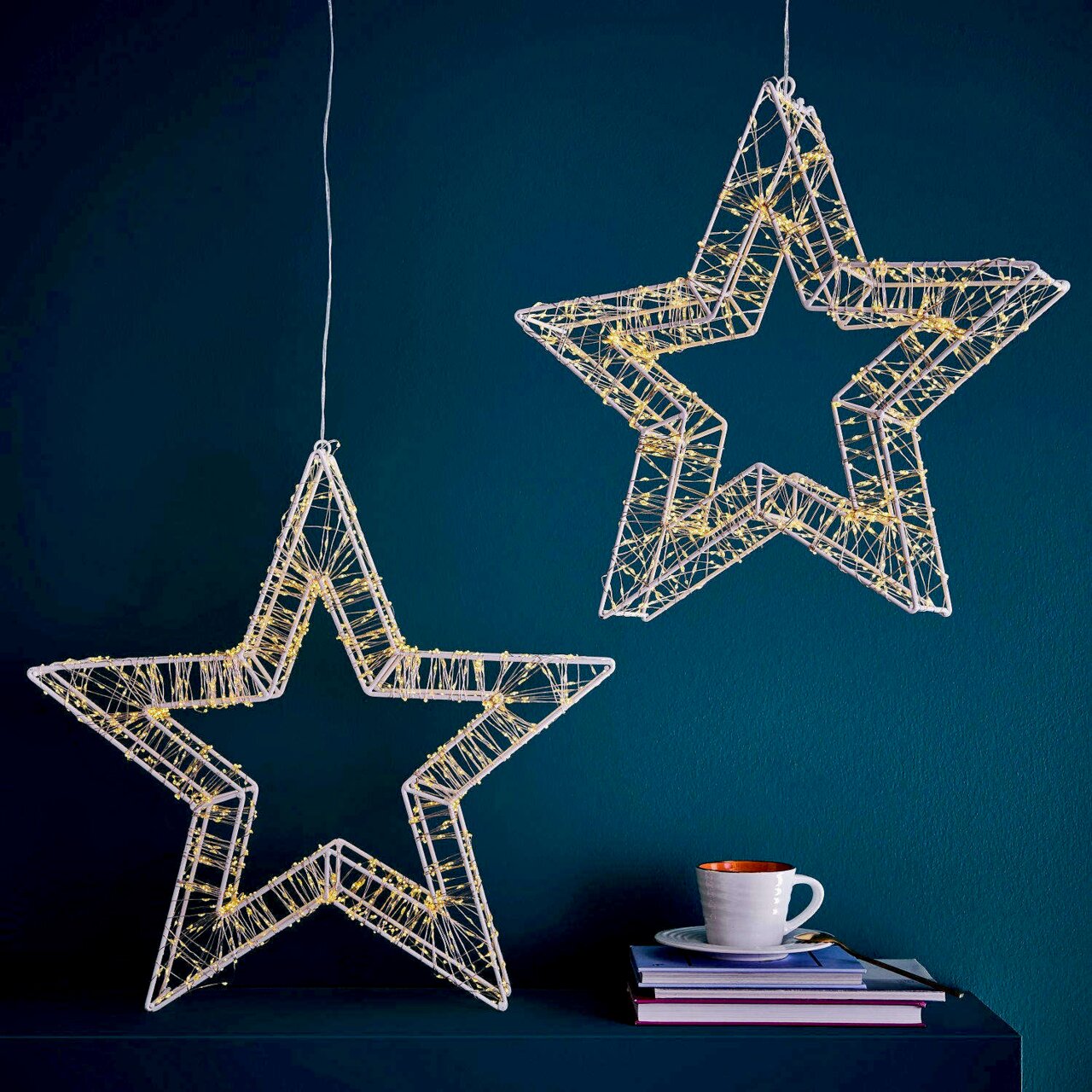 Zwei hängende LED-Sterne mit 960 LEDs, die in einem modernen Raum vor einer dunkelblauen Wand leuchten. Perspektive von vorne.