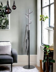Freistehende Garderobenständer/kleiderständer in Schwarz und Silber mit mehreren Haken und rundem Standfuß, seitliche Perspektive im Wohnzimmer neben Sofa und Fenster.