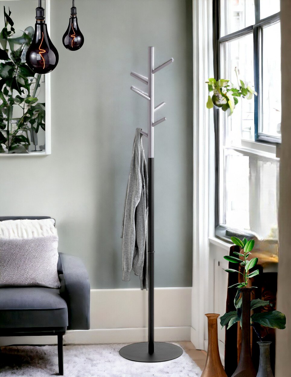 Freistehende Garderobenständer/kleiderständer in Schwarz und Silber mit mehreren Haken und rundem Standfuß, seitliche Perspektive im Wohnzimmer neben Sofa und Fenster.