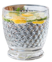 Close-up van een decoratief glas met schijfjes citroen en komkommer, gevuld met bruisend water.