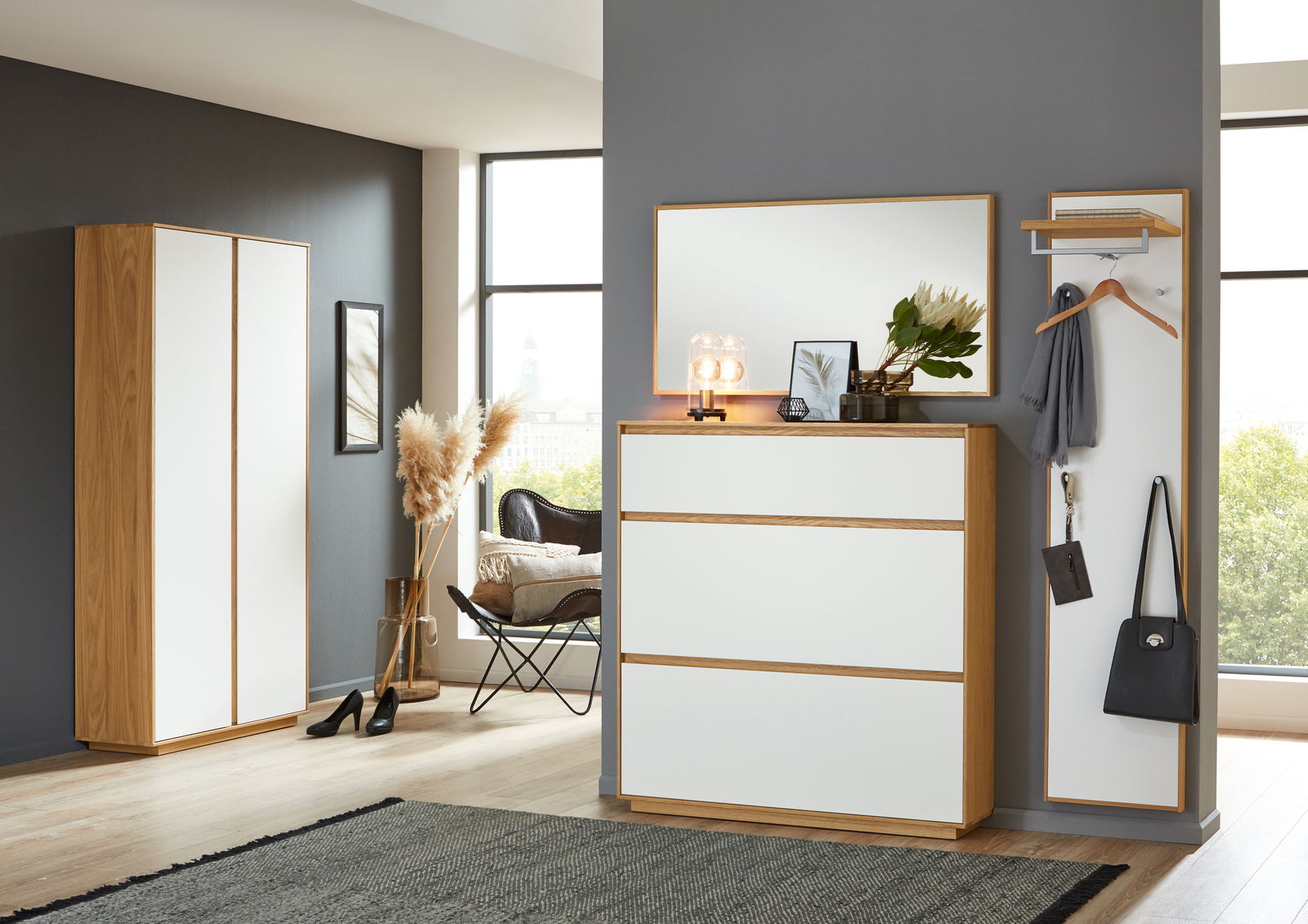 Moderne Garderobeneinrichtung mit weißem Schuhschrank, Spiegel und Garderobenpaneel in einem hellen Raum. Perspektive von vorne.