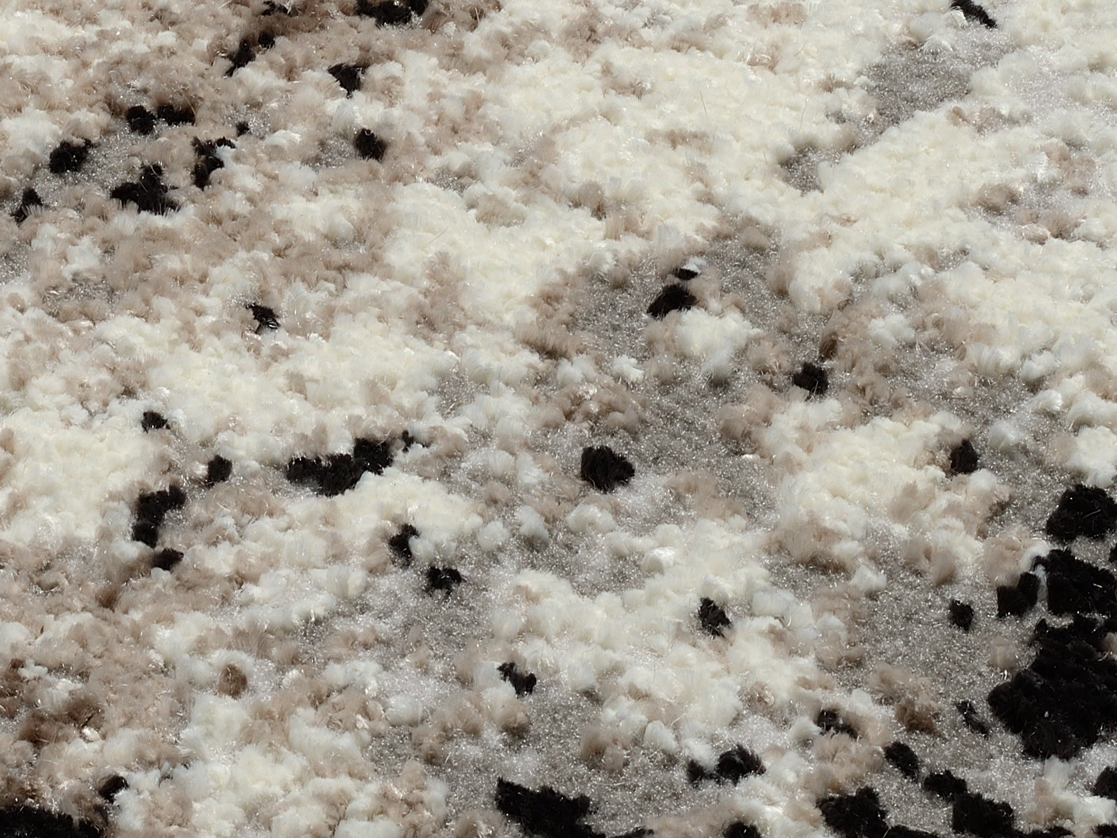 Nahaufnahme eines Designer Teppichs mit flauschiger Textur in Creme-, Beige- und Schwarztönen, von oben betrachtet.