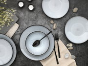 Vogelperspektive auf ein elegantes 12-teiliges Tellerset mit dezentem Muster, umgeben von Besteck, Kerzen und Dekoration auf einem dunklen Tisch.