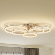 Moderne LED-Deckenleuchte mit vier leuchtenden, kristalloptischen Ringen in warmweiß, Ansicht von unten in leicht seitlicher Perspektive an der Zimmerdecke