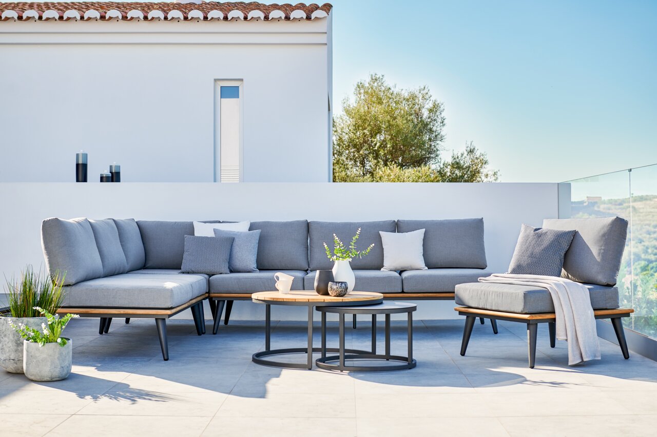 Niehoff-Garden Loungetisch SERRA Moderne Ecklounge mit grauen Kissen und zwei runden Loungetischen auf einer Terrasse, seitliche Perspektive.