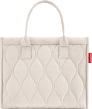 Beige gewatteerde draagtas met ovaal quiltpatroon en twee hengsels, close-up van de voorkant tegen een witte achtergrond