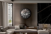 Moderne Wanduhr mit römischen Ziffern und Zahnrädern, frontal an einer Wohnzimmerwand montiert.