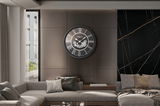 Moderne Wanduhr mit römischen Ziffern und Zahnrädern, frontal an einer Wohnzimmerwand montiert.