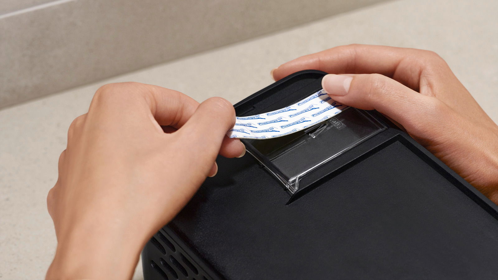 Nahaufnahme einer Person, die ein Klebepad auf die Rückseite eines schwarzen Duschkorbs anbringt.