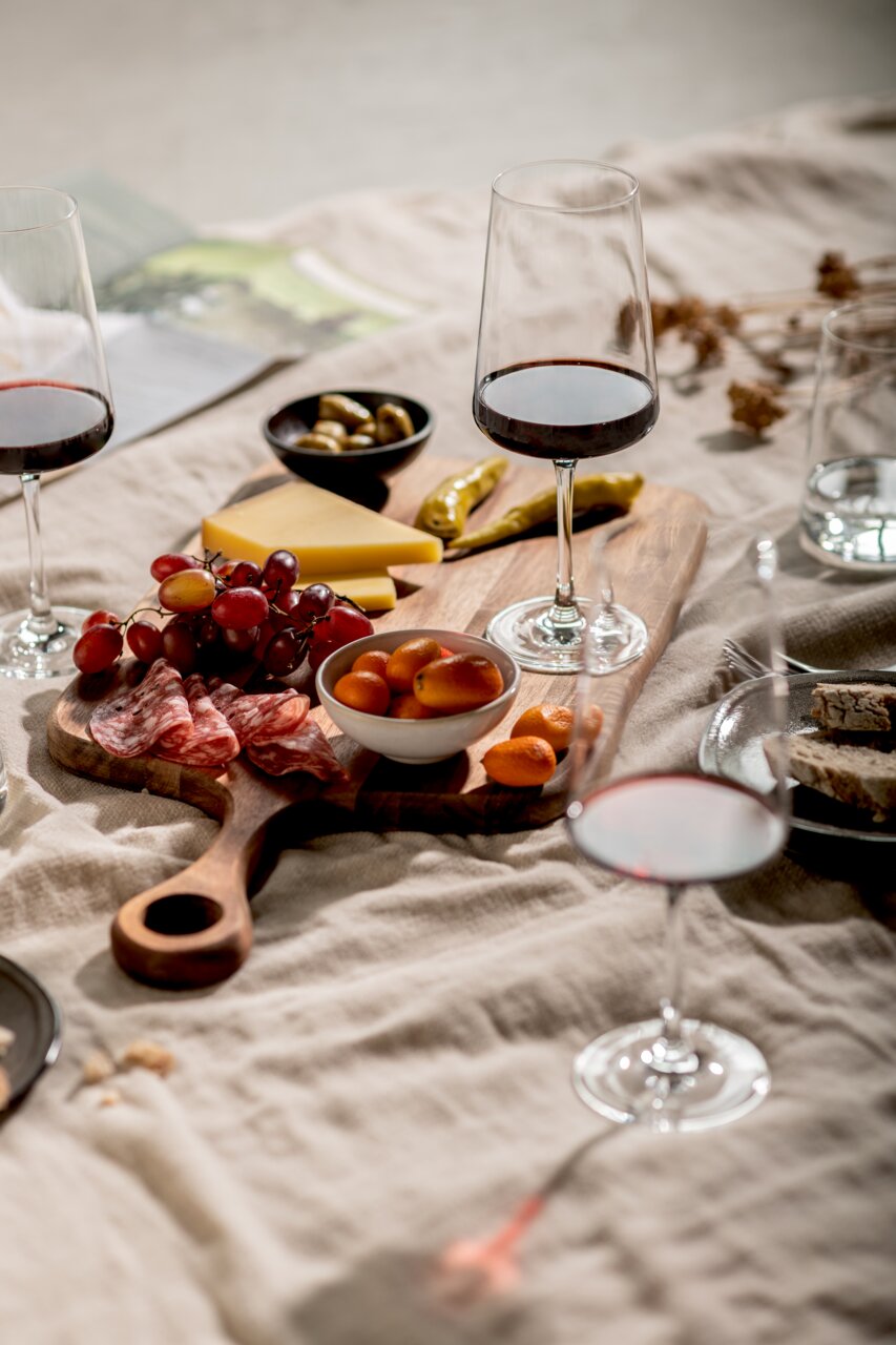 SCHOTT ZWIESEL Rotweinglas 4er-Set MIOVINO Ein stilvolles Rotweinglas-Set auf einem Tisch mit einer Auswahl an Käse, Trauben und Wurst, aus der Vogelperspektive fotografiert.