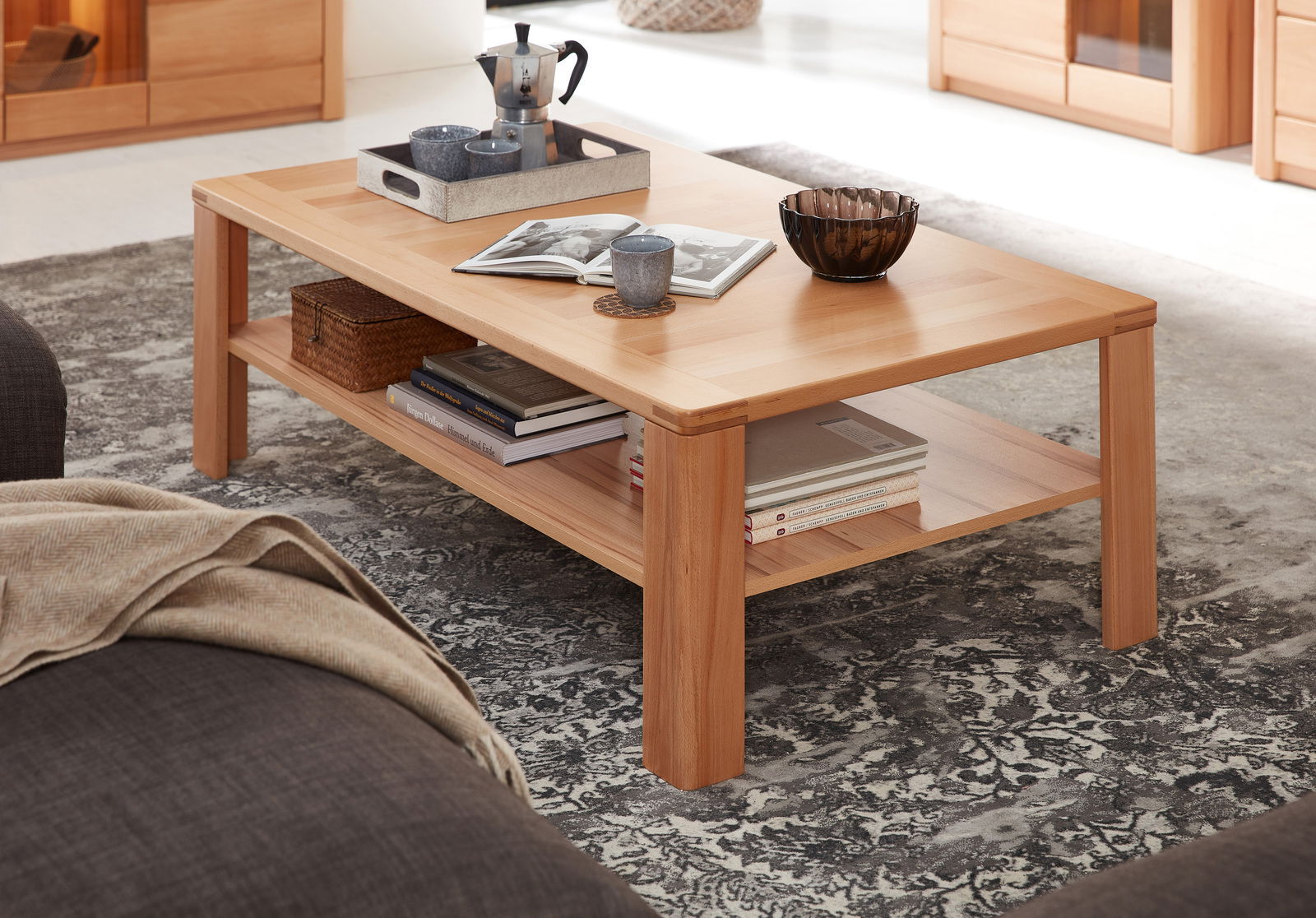 Moderner Couchtisch aus Holz mit Ablage, dekoriert mit Büchern, Tassen und einer Schale, seitliche Perspektive