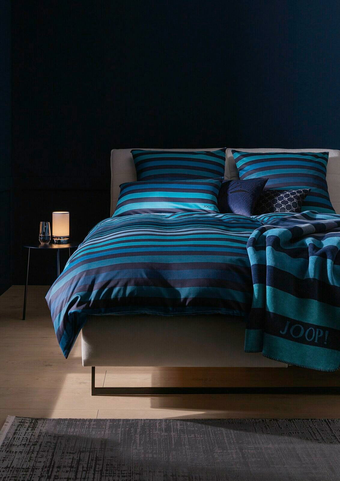 Bettwäsche-Set in Blau- und Schwarztönen mit Streifenmuster, frontal fotografiert auf einem Bett mit dekorativen Kissen.