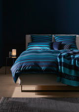 Bettwäsche-Set in Blau- und Schwarztönen mit Streifenmuster, frontal fotografiert auf einem Bett mit dekorativen Kissen.