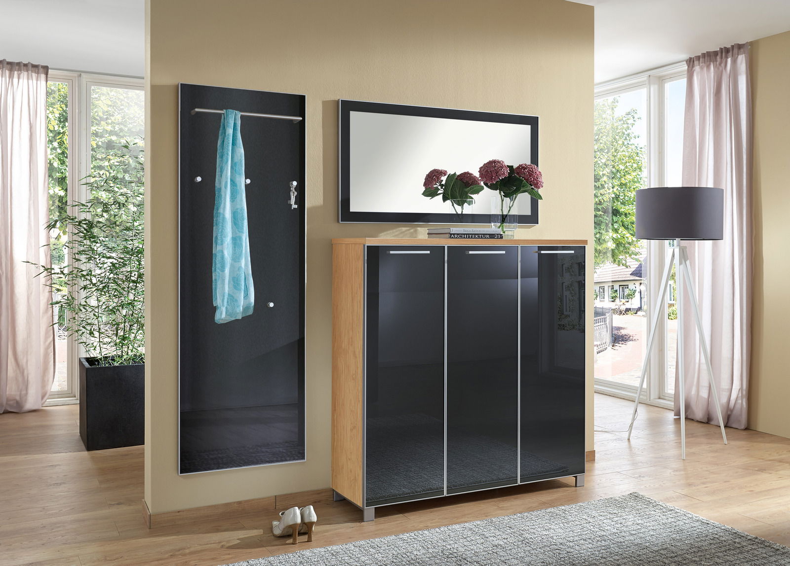 Garderoben-Set bestehend aus einem schwarzen Wandpaneel mit Kleiderstange und Haken, einem Spiegel und einem Schrank mit glänzenden Türen, seitliche Perspektive.