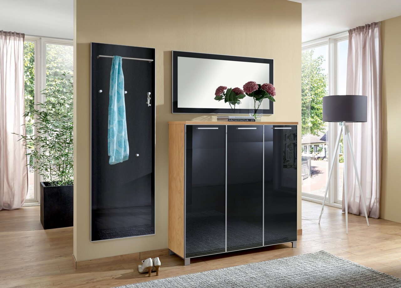 Garderoben-Set bestehend aus einem schwarzen Wandpaneel mit Kleiderstange und Haken, einem Spiegel und einem Schrank mit glänzenden Türen, seitliche Perspektive.