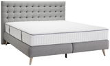 Graues Boxspringbett mit gestepptem Kopfteil und weißer Matratze, seitliche Perspektive