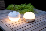 Twee ronde CHERRY-lampen op accu van New Garden op een houten tafel, waarvan één met een haak om op te hangen, gefotografeerd vanuit een zijaanzicht.
